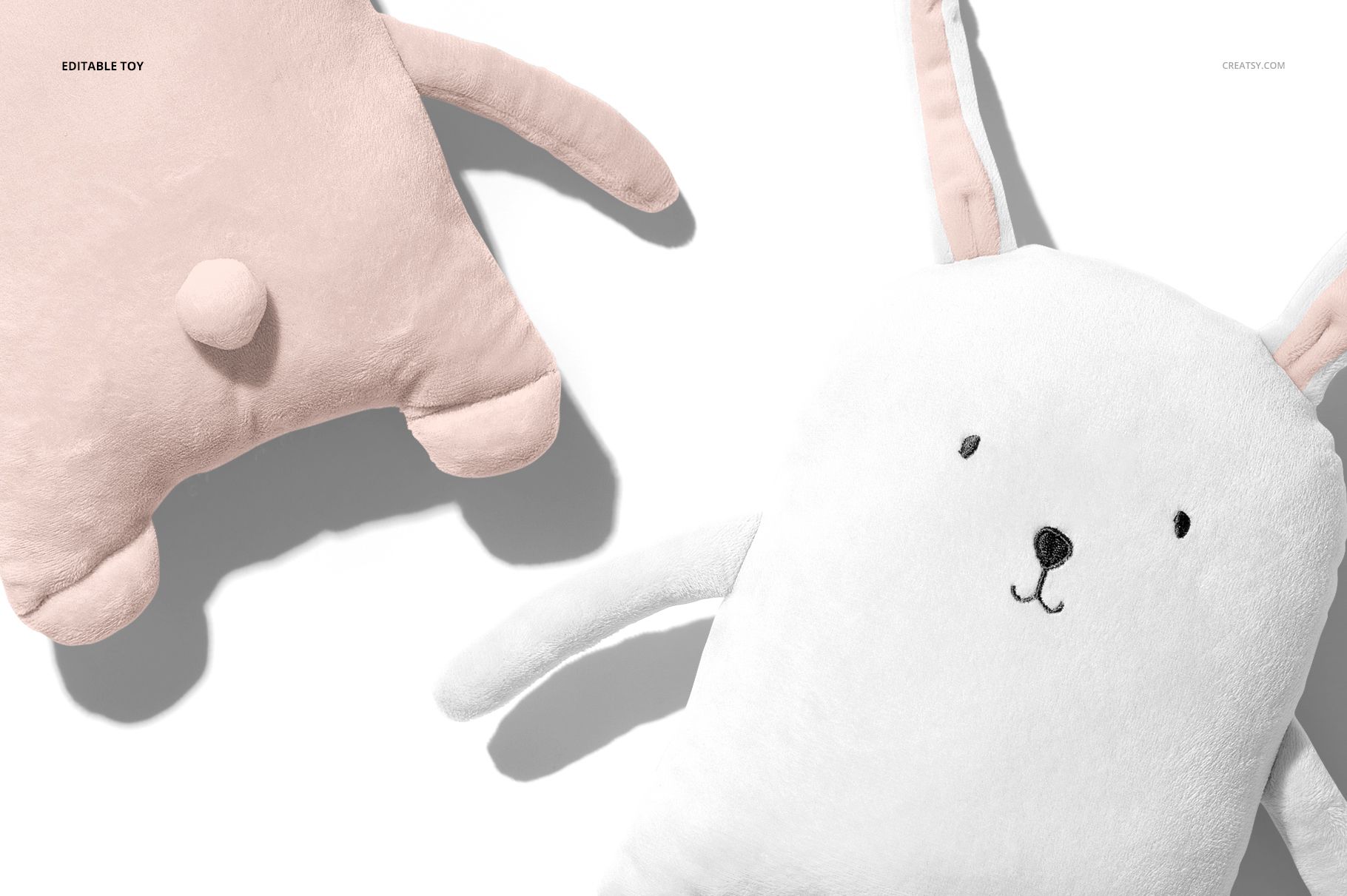 Close-up of baby wearable blanket mockup featuring a white bunny design and a pink plush toy, both on a light surface.
