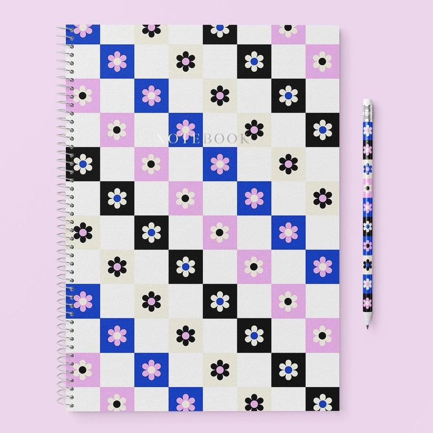 Stationery mockup featuring a spiral notebook with a checkered floral cover in black, blue, pink, and white, next to a matching pencil on a pastel pink background.