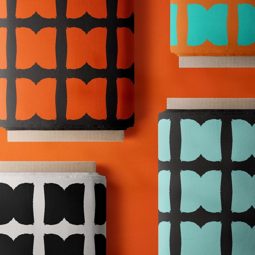 Fabric bolt mockup showing four rolls of fabric with bold geometric patterns in black, orange, white, and turquoise colors.