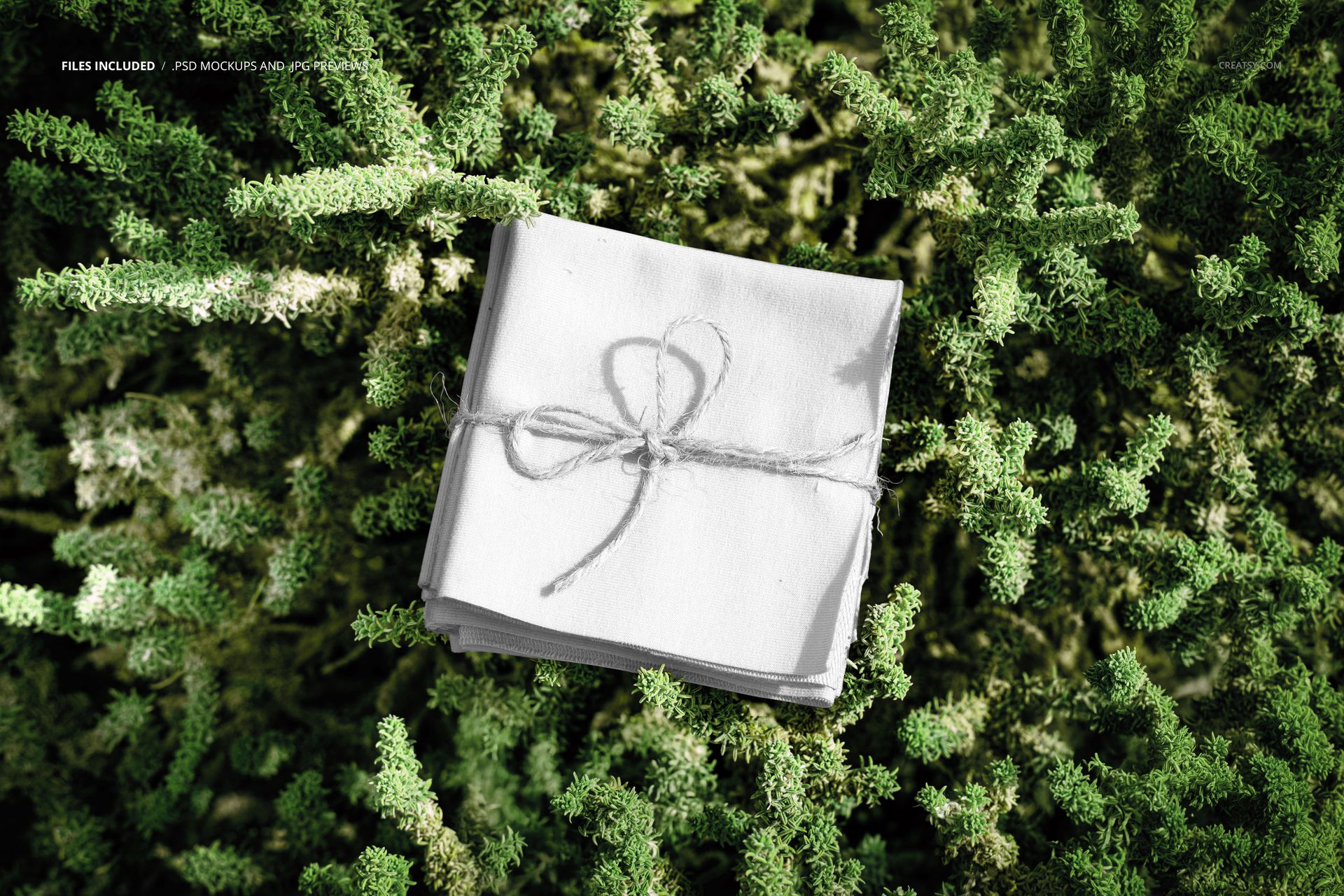 Stack of square fabric pieces tied with string, placed on dense green foliage, top view, fabric mockup scene.