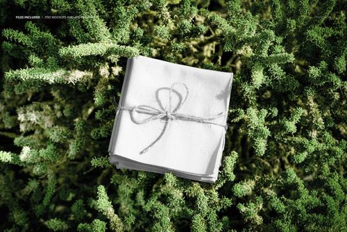 Stack of square fabric pieces tied with string, placed on dense green foliage, top view, fabric mockup scene.