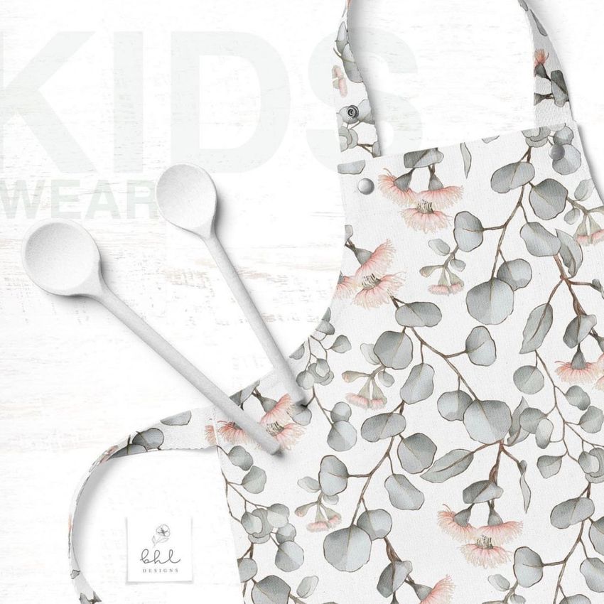 Kids apron mockup featuring a white apron with a eucalyptus leaf and pink flower pattern, shown with two white wooden spoons.