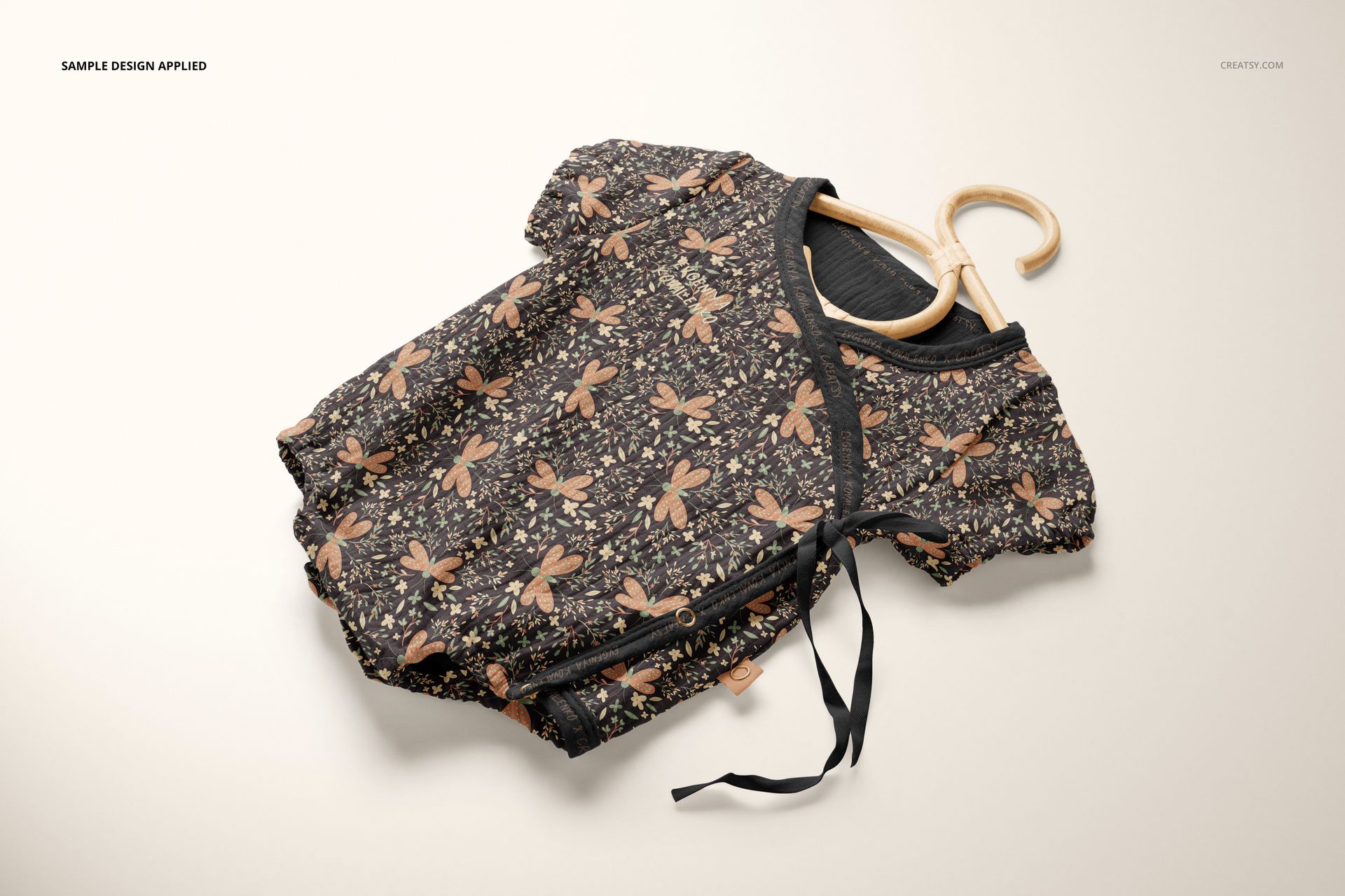 Top view of a muslin onesie mockup on a hanger, decorated with a black background and botanical print.