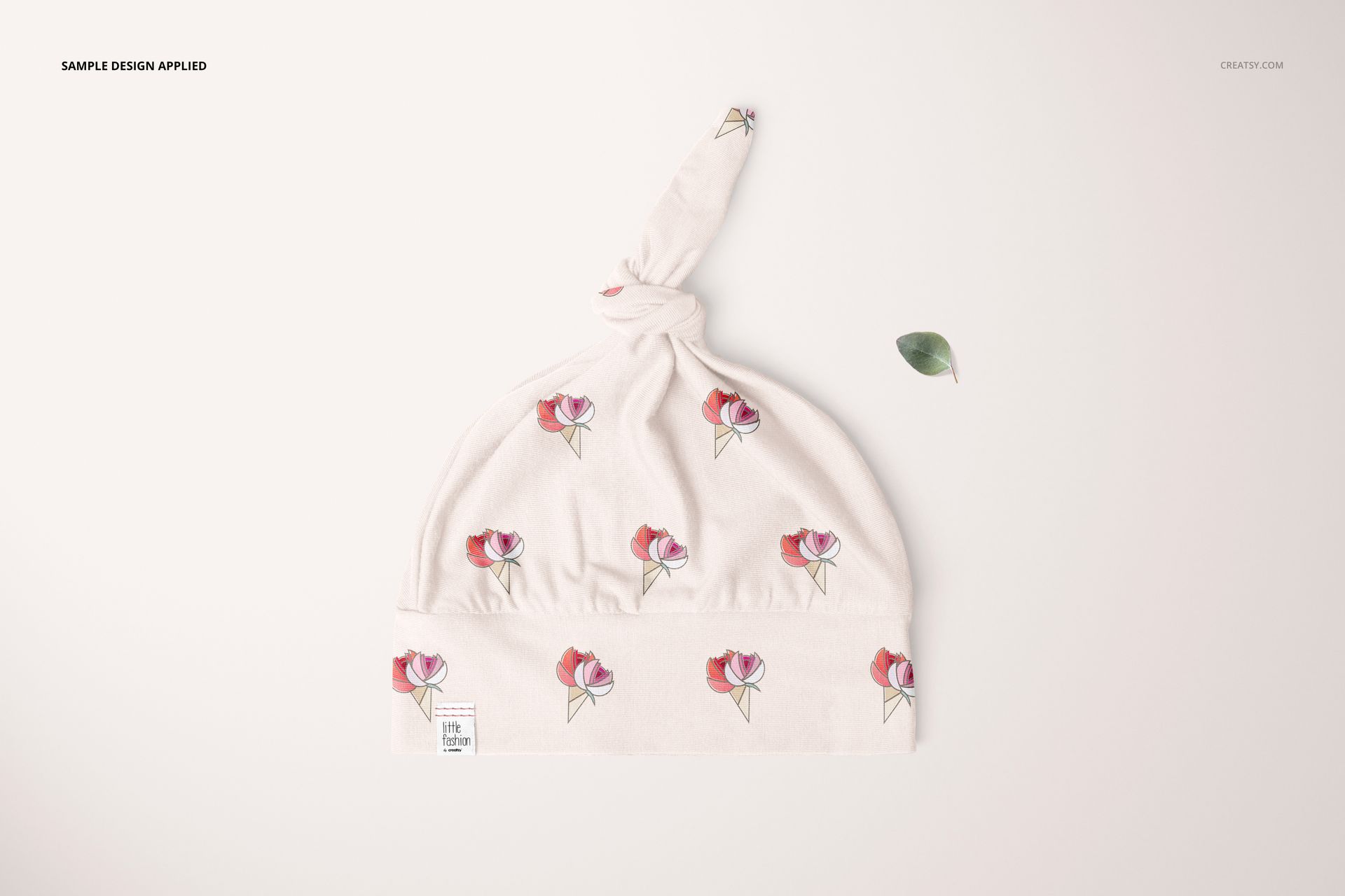 Top view of a soft baby hat mockup featuring pink flower prints and a knotted top, set against a pale surface.