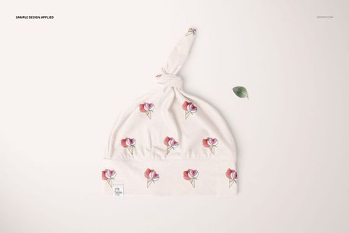 Top view of a soft baby hat mockup featuring pink flower prints and a knotted top, set against a pale surface.