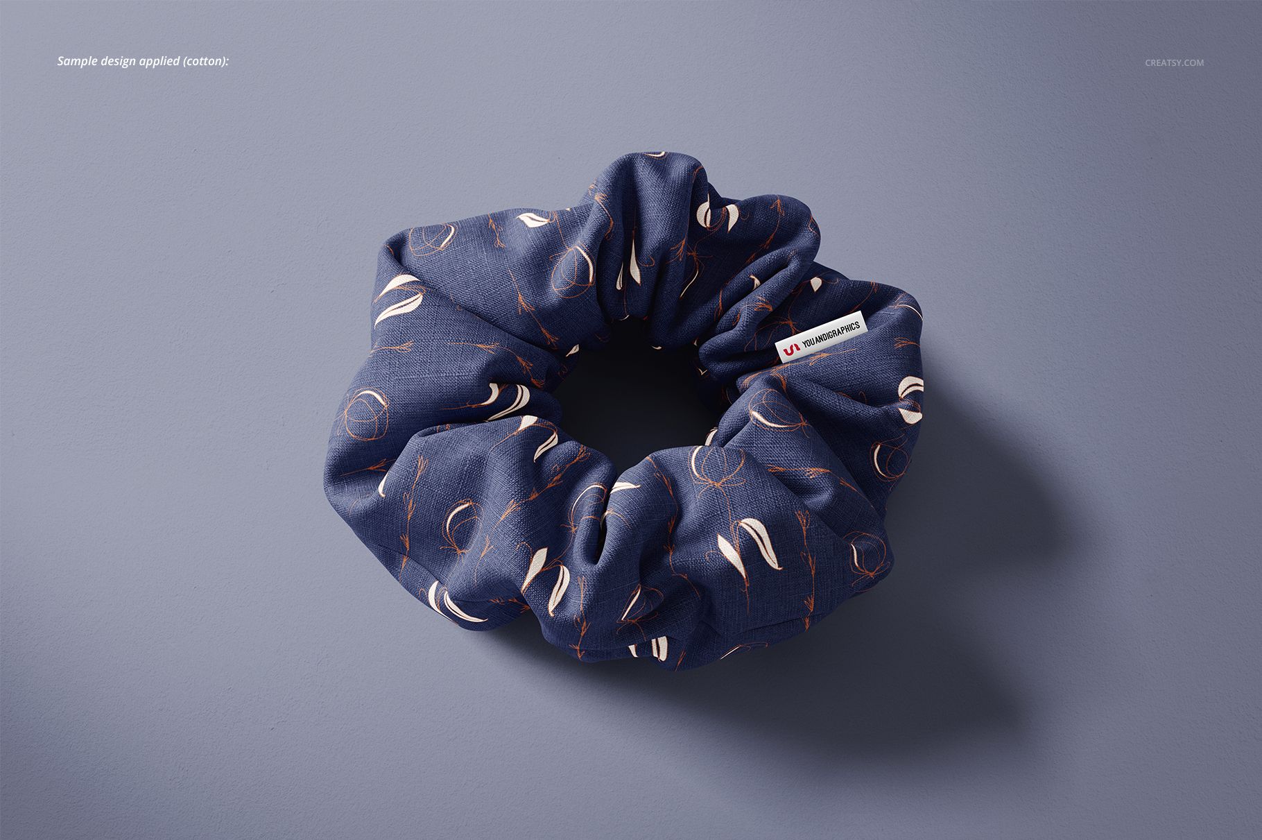 Cotton hair scrunchie mockup with a blue fabric featuring abstract white and orange patterns, shown on a gray background.