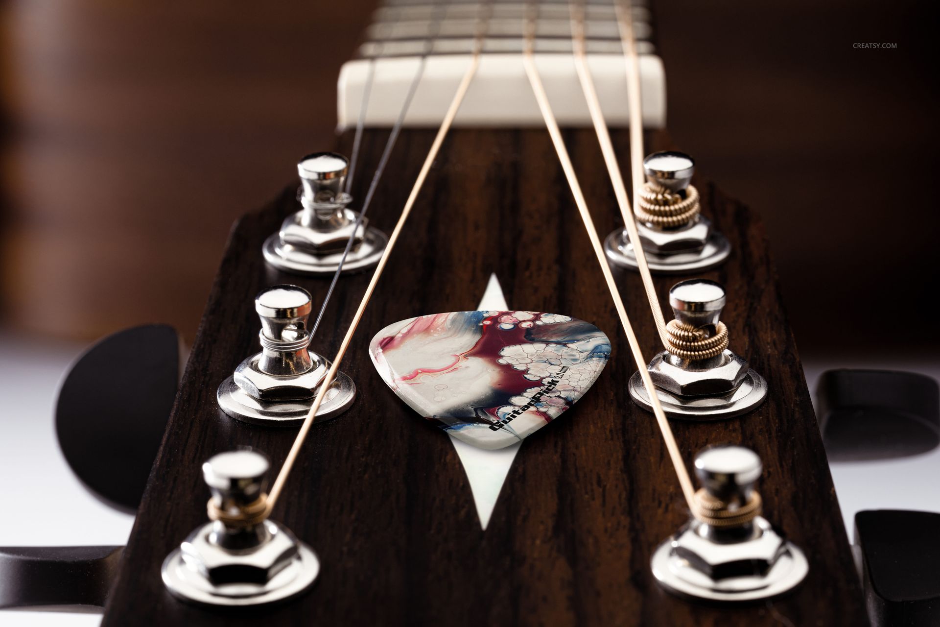 PSD mockup showing a detailed guitar headstock with chrome tuners and a multicolored pick positioned near the center.