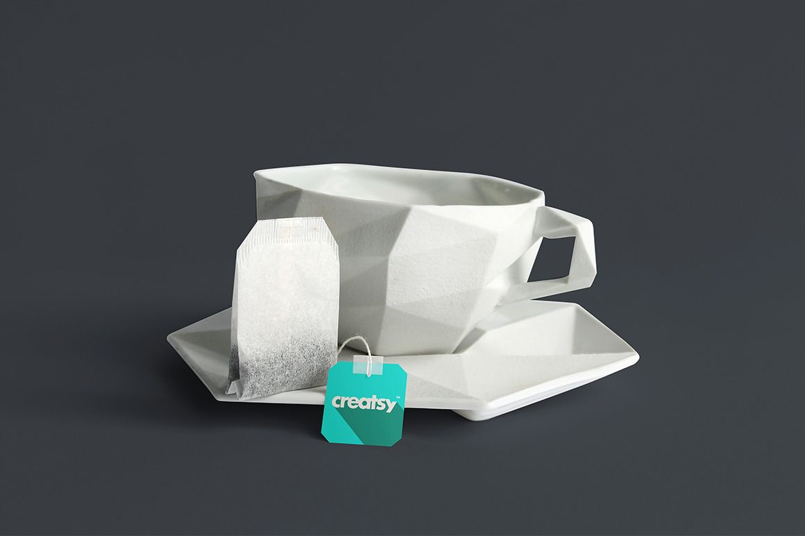 PSD mockup of a polygonal white tea cup set with tea bag and teal tag, shown against a dark gray backdrop.