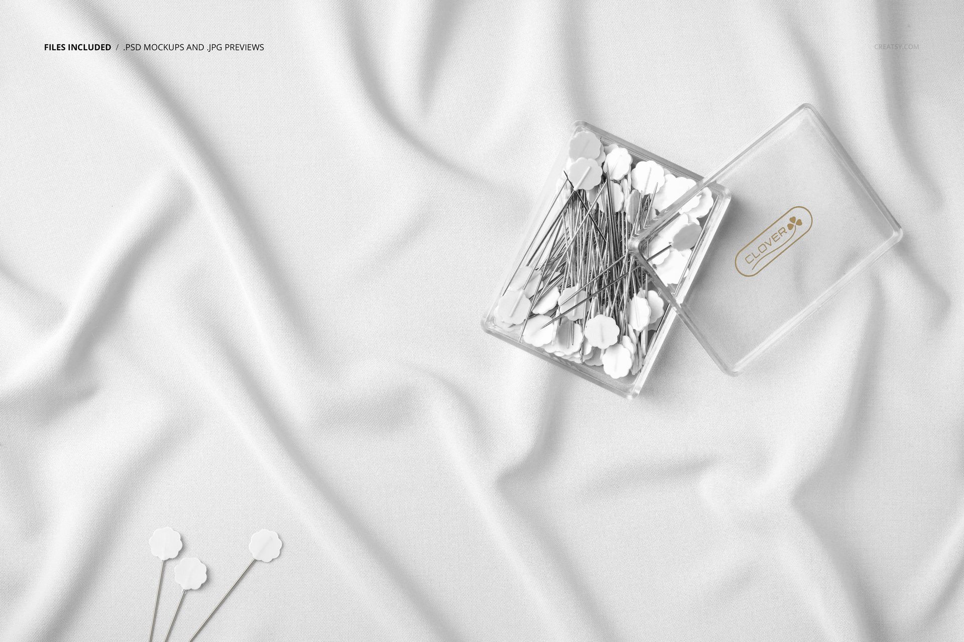 Wrinkled white fabric mockup shown from above with a clear plastic box containing metal pins and loose pins nearby.