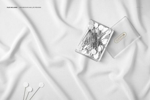Wrinkled white fabric mockup shown from above with a clear plastic box containing metal pins and loose pins nearby.