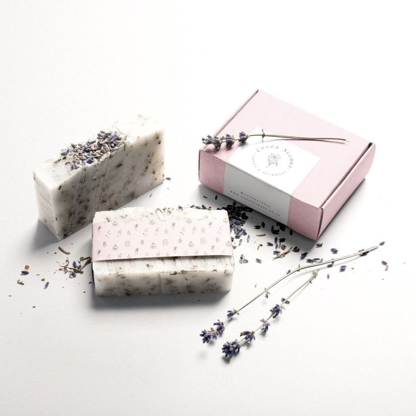 Packaging and wrapping mockup featuring a pink box with a white sticker, two bars of soap, and dried lavender on a white surface.