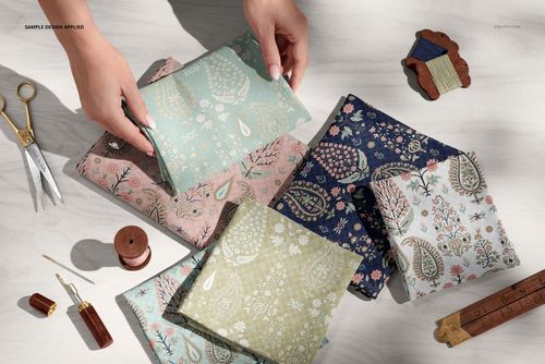 Hands arranging colorful jersey fabric pieces on a worktable with scissors, thread, and ruler, in a PSD mockup scene.