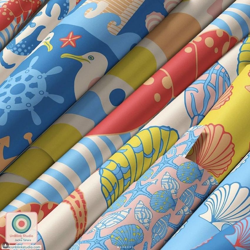 Paper wallpaper mockup featuring several rolled sheets with colorful seashell and ocean-themed patterns in blue, red, and yellow tones.