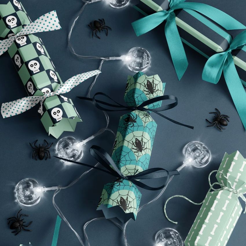 Halloween party cracker packaging mockup featuring patterned crackers with spiders, skulls, and geometric designs on a dark surface.