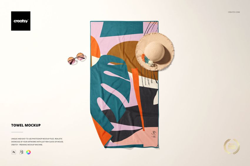 Top view of a rectangular beach towel mockup featuring bold abstract designs, placed beside a straw hat and sunglasses.