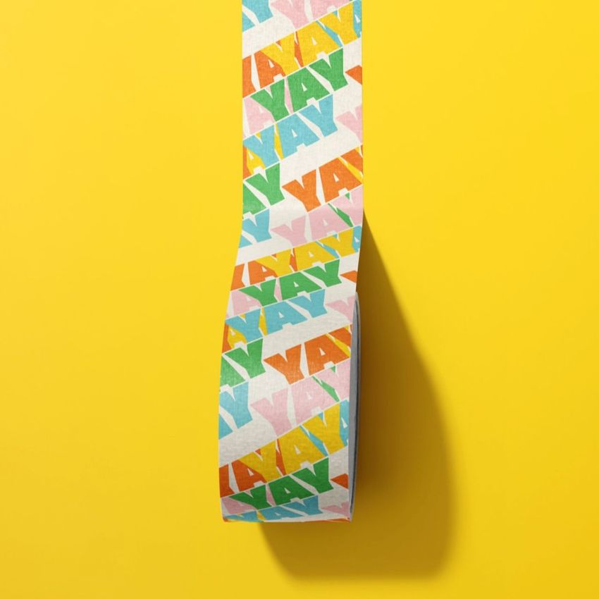 Close-up of a masking tape mockup featuring multicolored YAY lettering, set against a bright yellow backdrop.