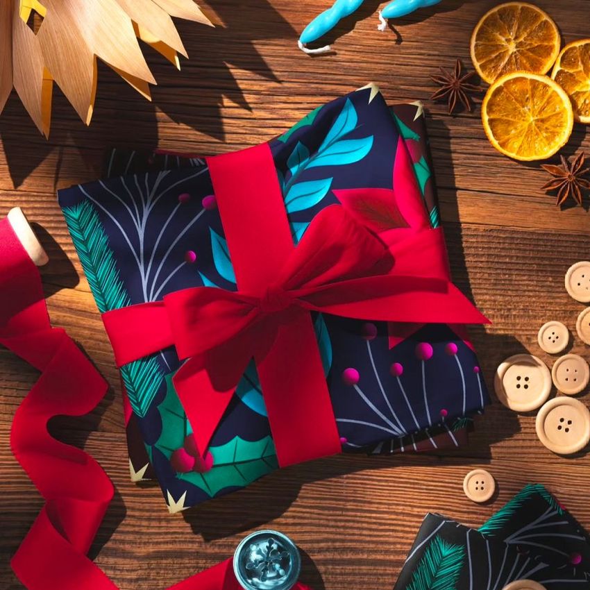 Christmas folded cotton fabric mockup featuring a bold botanical print, tied with a red ribbon on a rustic wooden table.