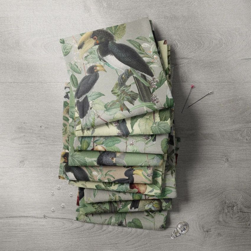 Fabric stack mockup featuring multiple folded textiles with a tropical bird and foliage pattern, displayed on a light wooden surface.