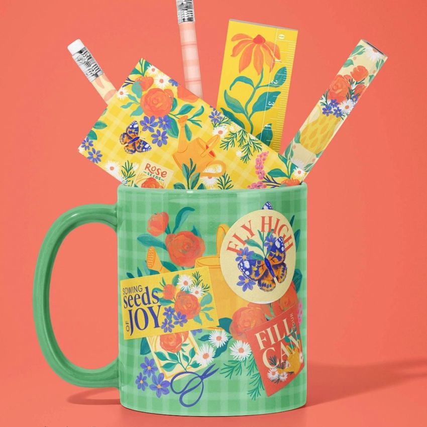 Mug mockup with a green gingham pattern, filled with colorful floral stationery items and pencils, set against a coral background.