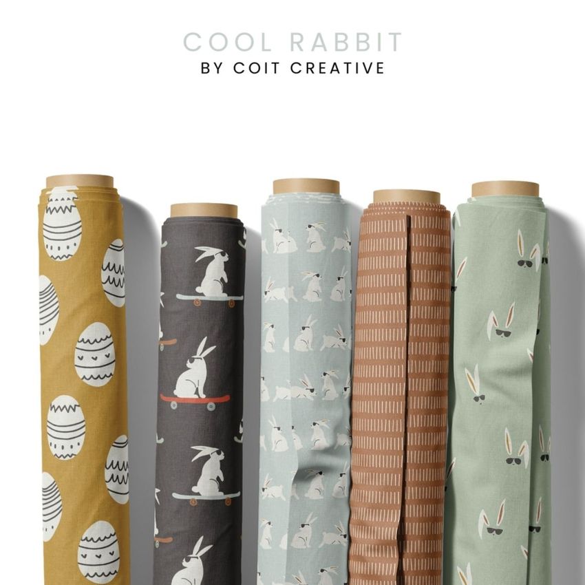 Fabric rolls mockup featuring five upright rolls with playful rabbit and egg patterns in muted earth tones on a white background.