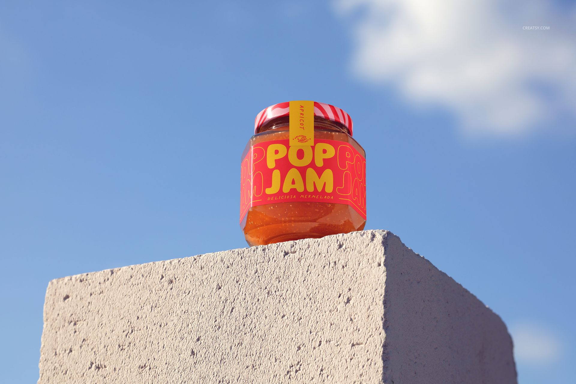 Front view of a jam jar mockup with bright orange jam and bold label, set atop a rough gray block outdoors.