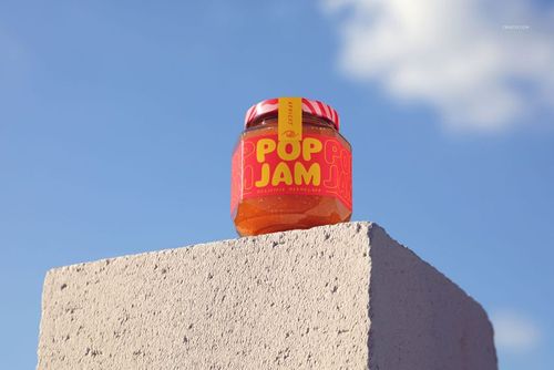 Front view of a jam jar mockup with bright orange jam and bold label, set atop a rough gray block outdoors.