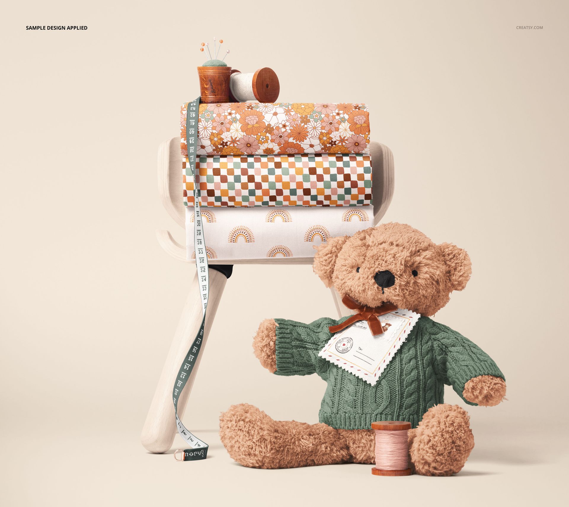 Cotton fabric mockup showing patterned rolls on a stool, with a plush teddy bear and sewing accessories in the scene.