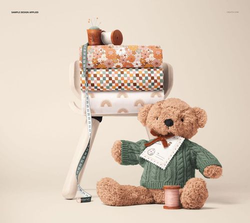 Cotton fabric mockup showing patterned rolls on a stool, with a plush teddy bear and sewing accessories in the scene.