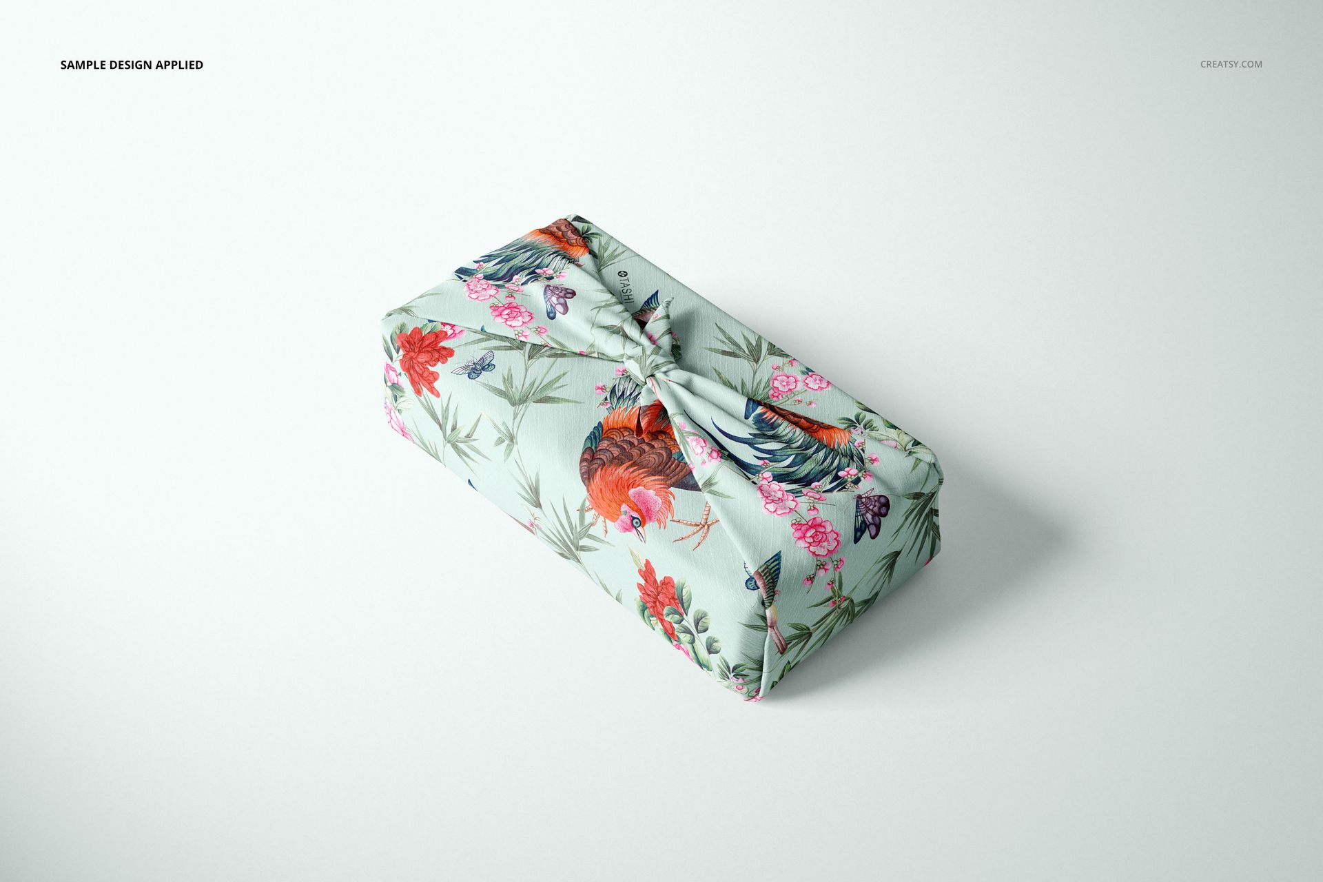 Furoshiki fabric wrap mockup featuring a pastel blue textile with vibrant flowers and rooster design, top view.