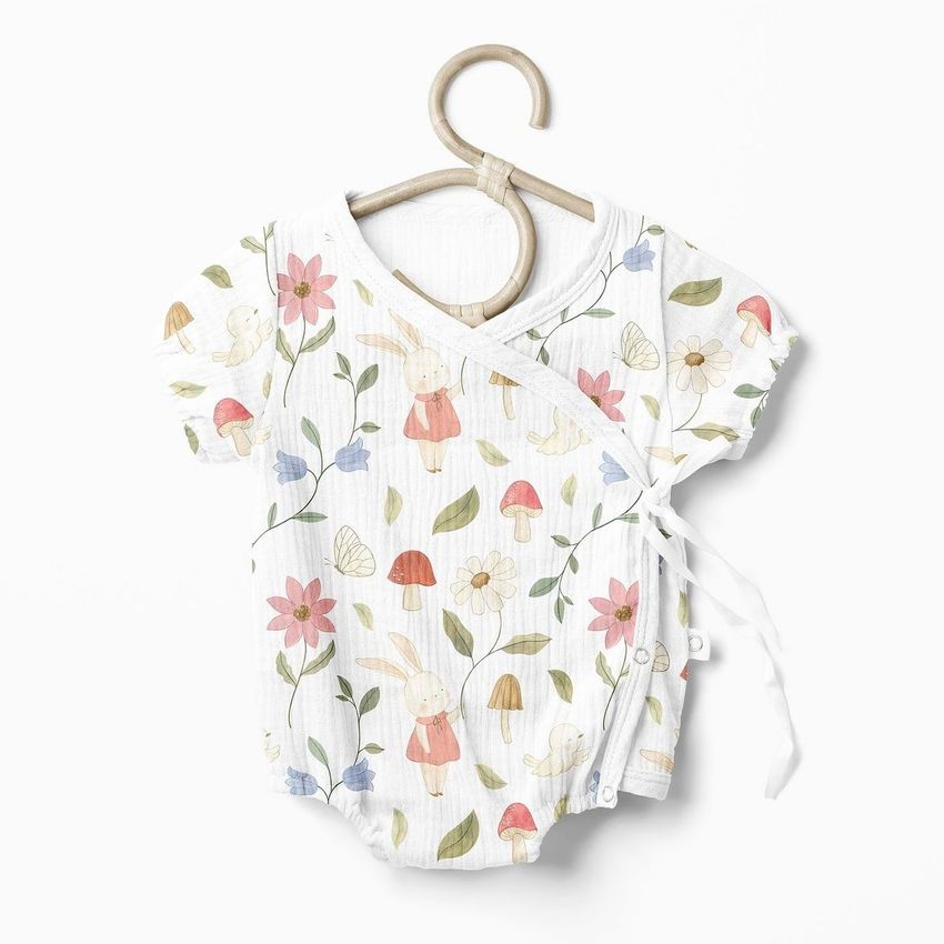 Muslin onesie mockup featuring a white baby bodysuit with a bunny and floral pattern, displayed on a wooden hanger against a light background.