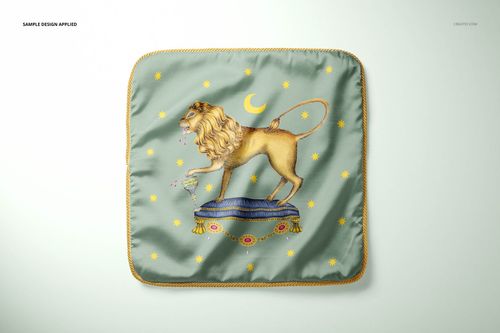Square silk pillow mockup with gold braid trim, lion motif, crescent moon, and star pattern on green fabric, overhead angle.