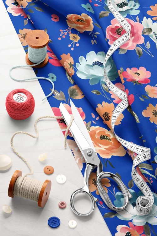 Blue cotton fabric mockup featuring vibrant flower designs, sewing scissors, tape measure, spools of thread, and buttons.