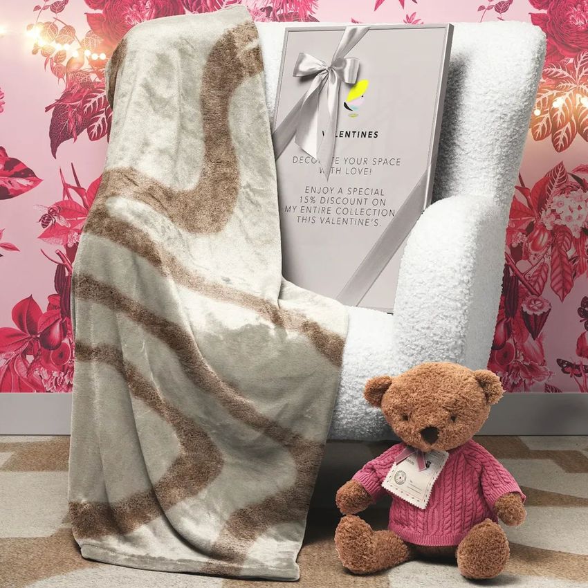 Christmas scene with a fleece blanket draped over a white armchair, a picture frame mockup, and a teddy bear in a pink sweater.