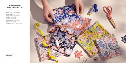PSD mockup showing floral jersey fabrics in layered folds, with props including thread, measuring tape, and sewing accessories.