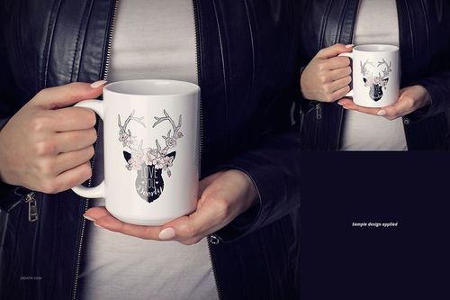Front view of a white ceramic mug with a floral deer illustration, held by a person wearing a black jacket.