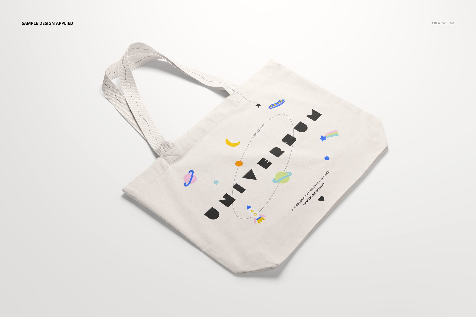White tote bag mockup displayed on a light background, decorated with colorful planets, stars, and bold black lettering.