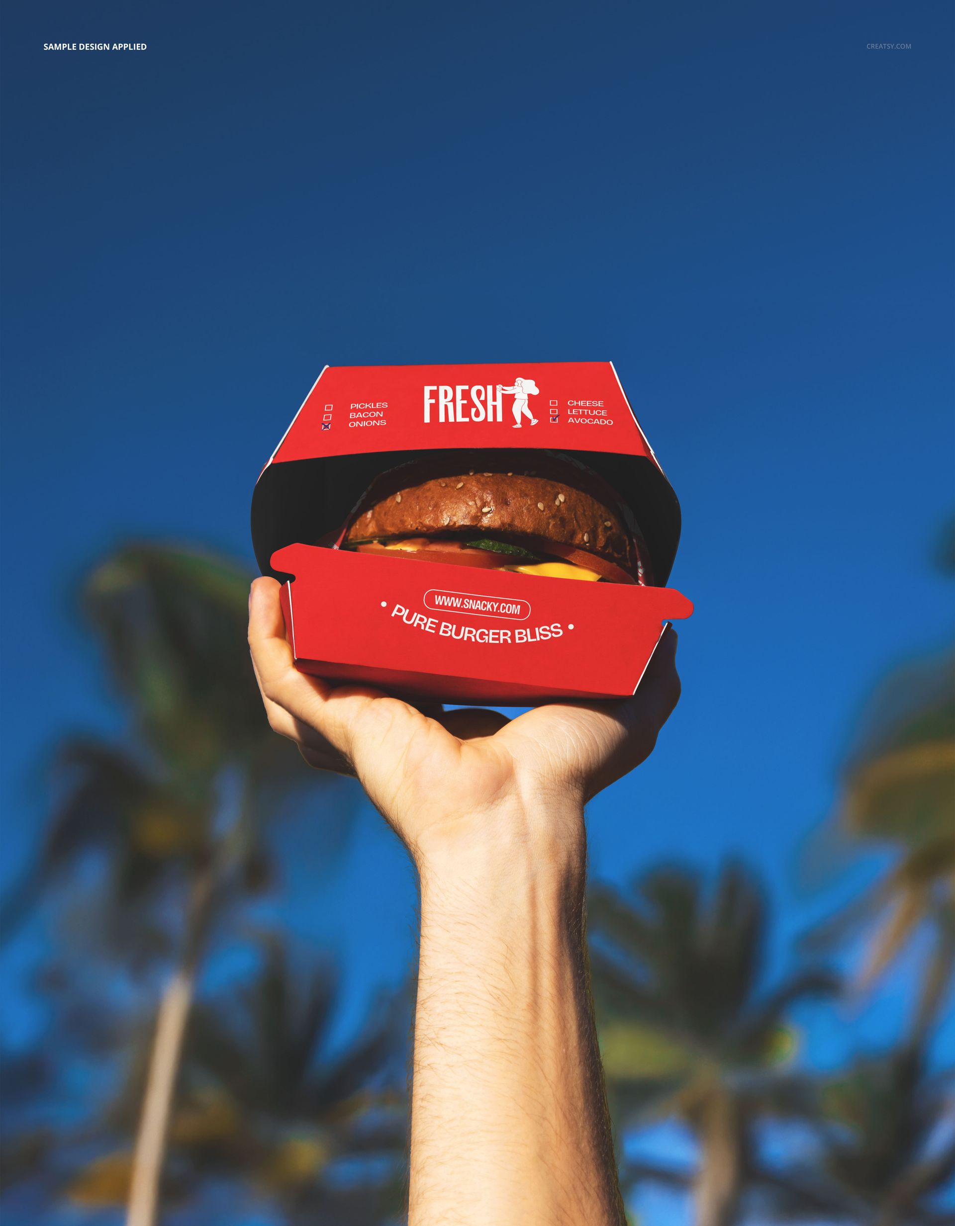Red burger packaging mockup held up by a hand, with a burger inside and palm trees in the background under blue sky.