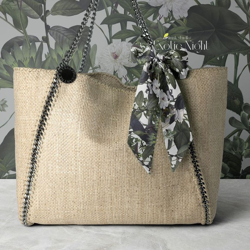 Twilly scarf mockup featuring a floral-patterned scarf tied to the handle of a woven beige handbag against a leafy wallpaper.