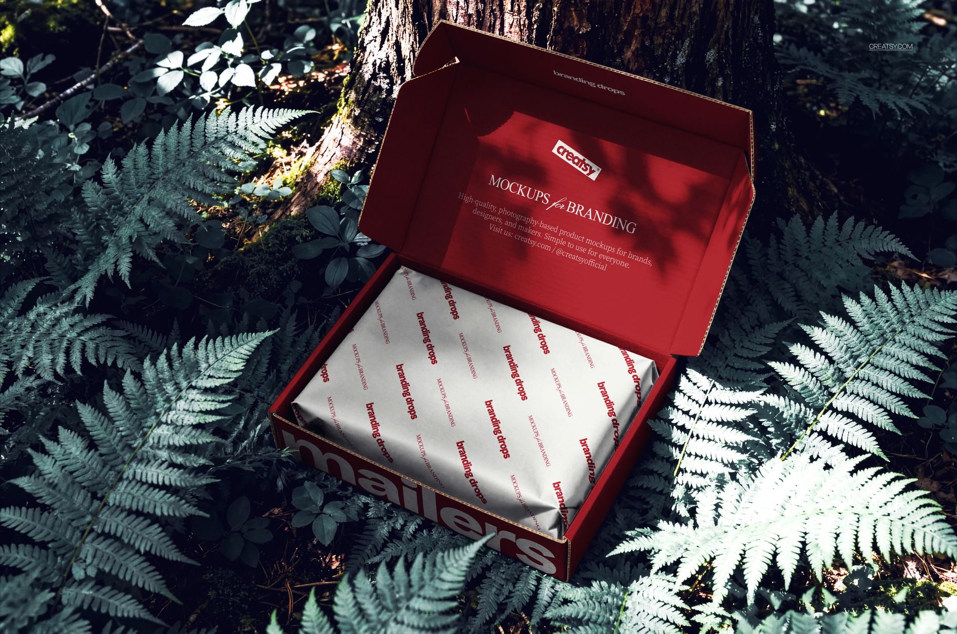 Red mailing box mockup displayed open on leafy forest ground, showing branded wrapping inside the box.