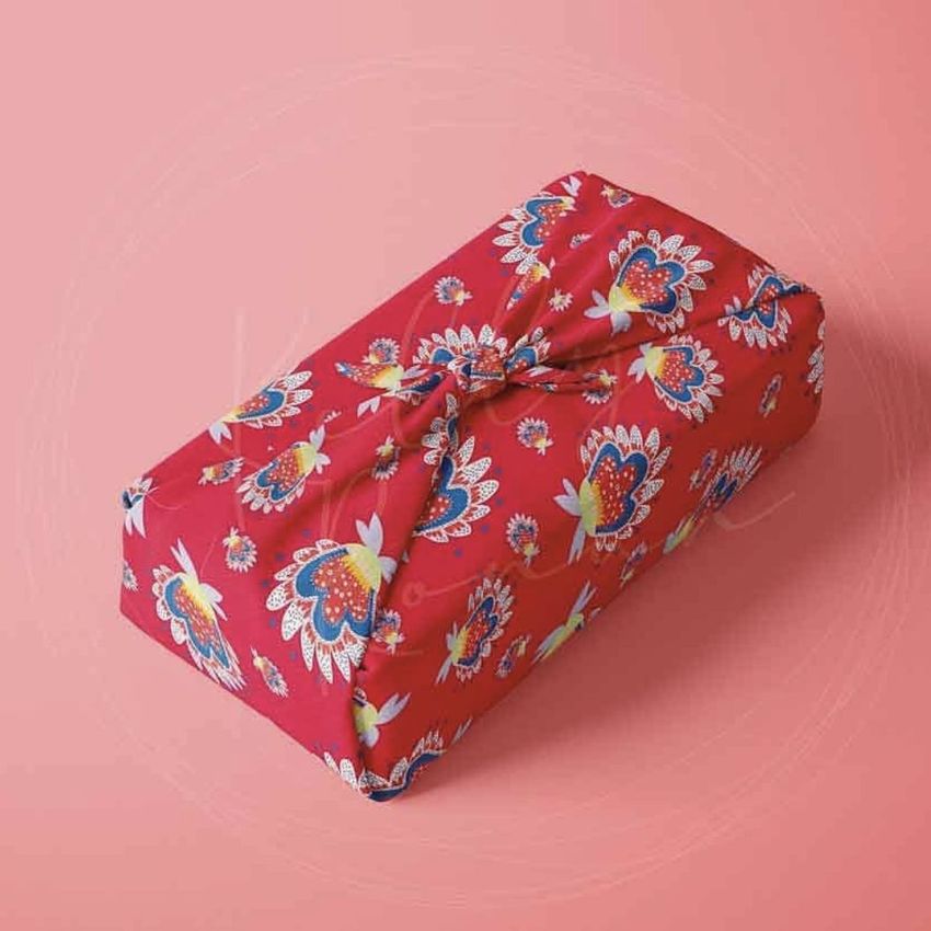 Furoshiki fabric wrap mockup featuring a rectangular box wrapped in red cloth with a colorful floral pattern on a pink background.