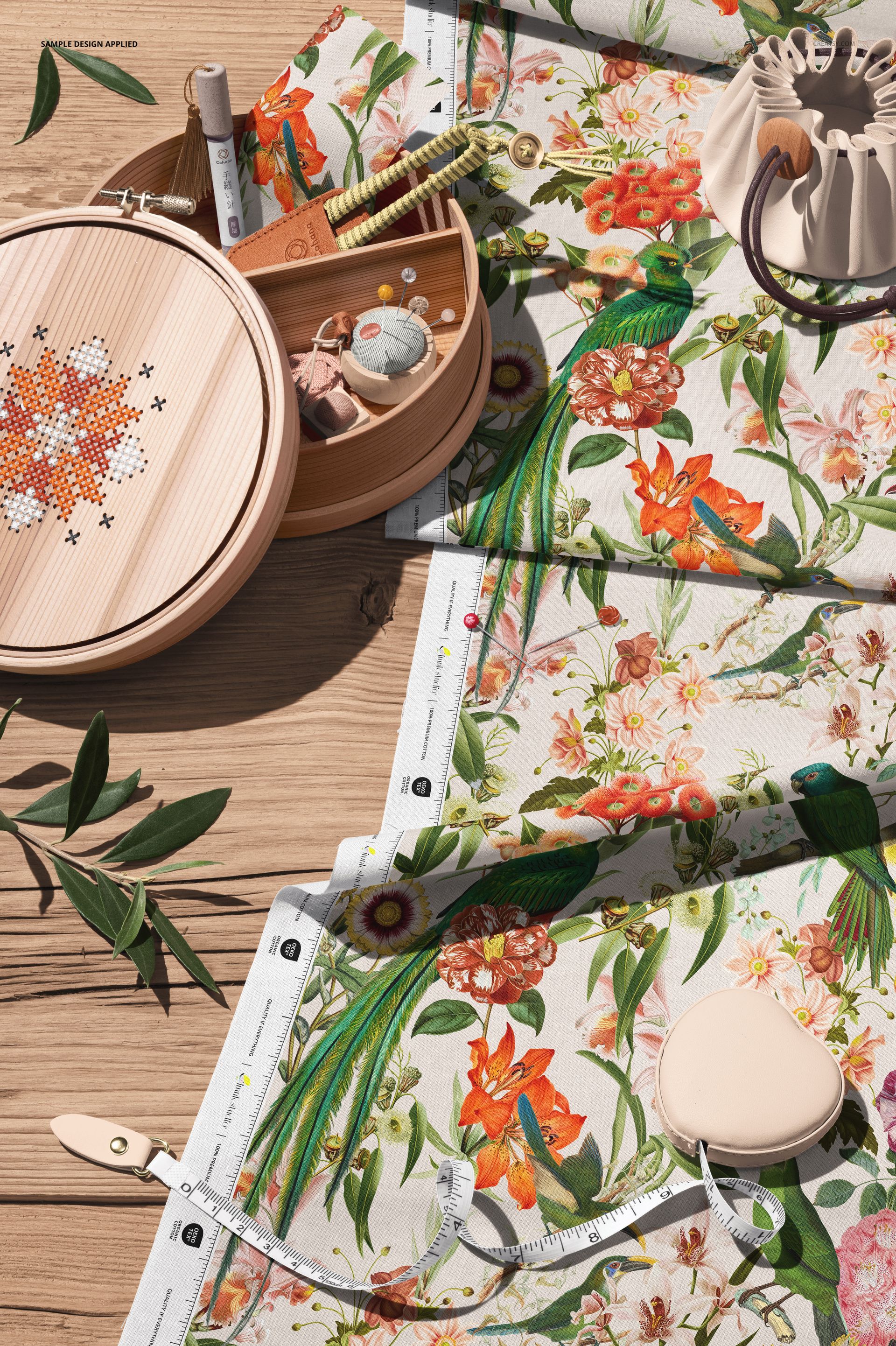 Floral and bird patterned cotton fabric mockup with embroidery kit, tape measure, and wooden box arranged on table.