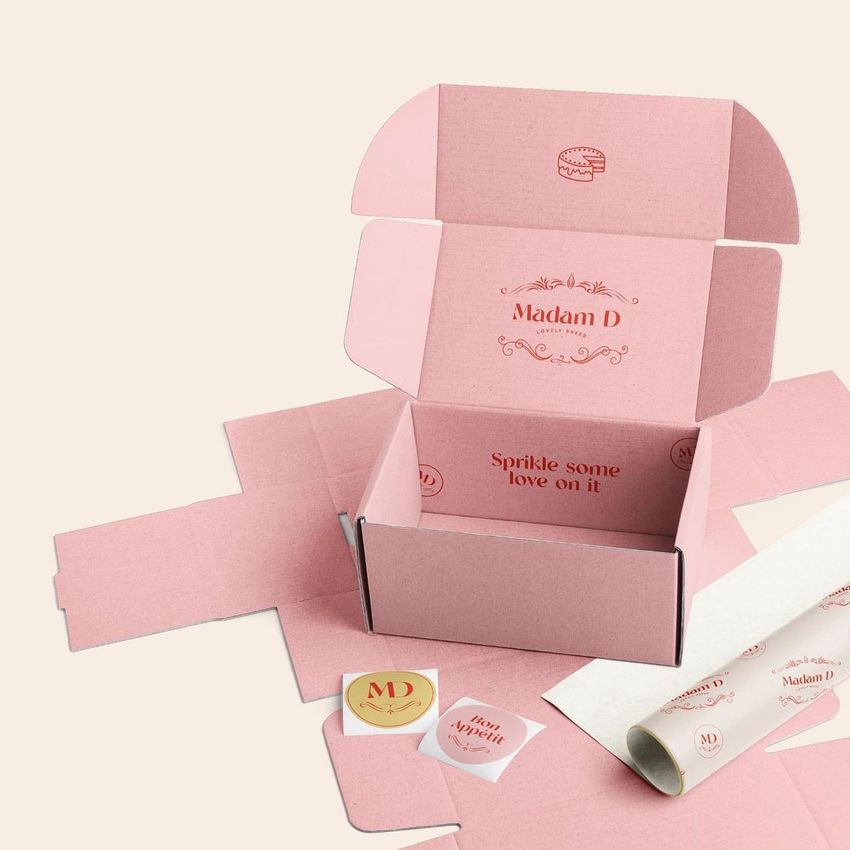 Mailing box mockup set featuring an open pink box with printed text, surrounded by unfolded packaging, stickers, and tissue paper.
