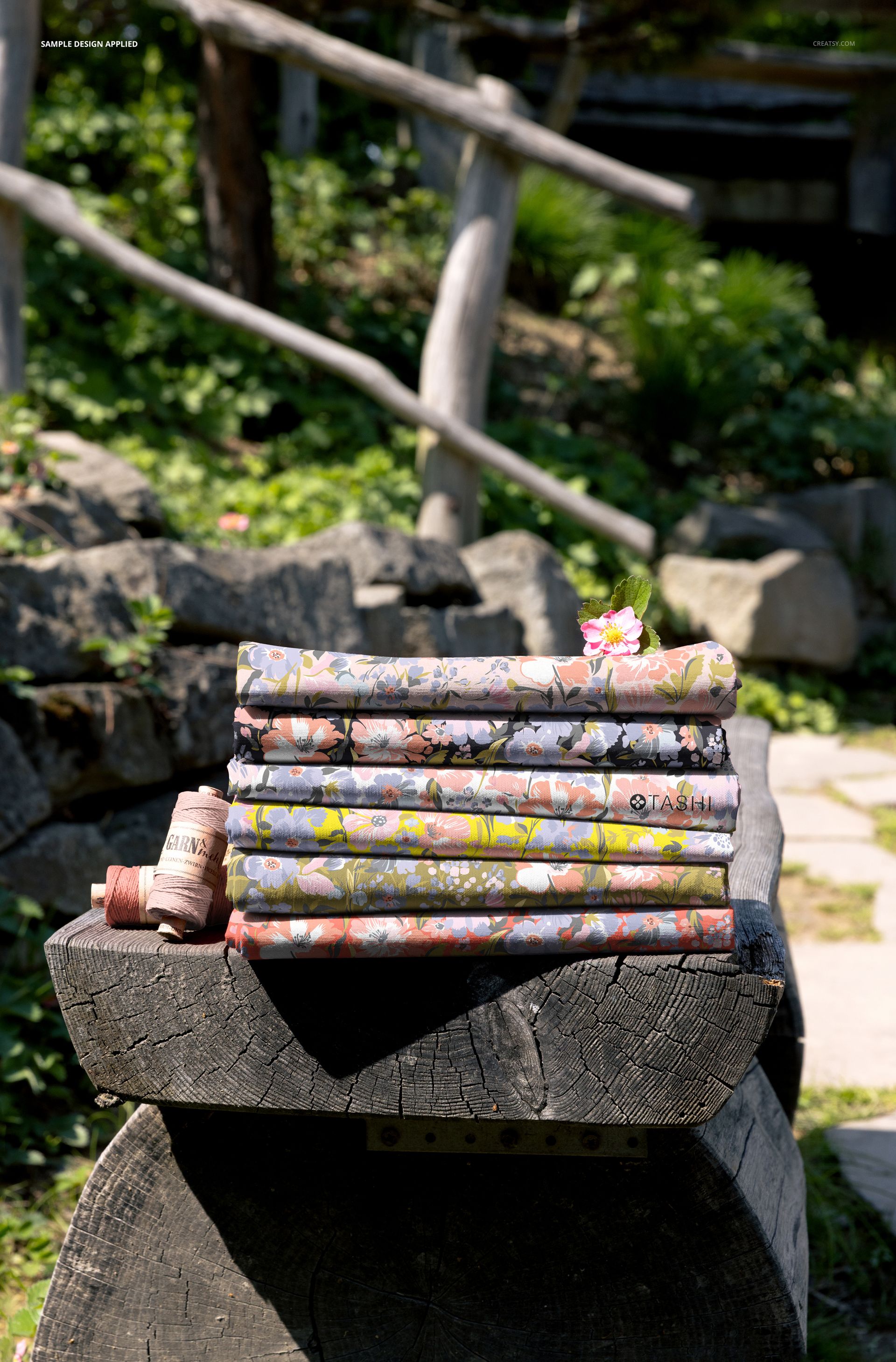 PSD mockup showing multiple folded fabric pieces with colorful designs on a natural wooden bench, outdoor scene.