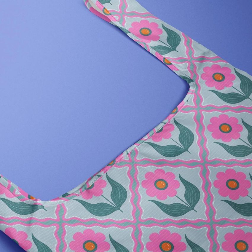 Reusable bag mockup featuring a retro floral pattern with pink flowers and green leaves on a light background, shown on a blue surface.