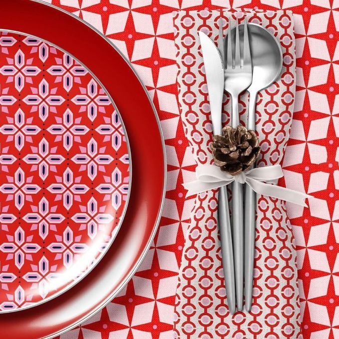 Christmas-themed plate, napkin, and tablecloth mockup featuring red and white geometric patterns, silverware, and a pinecone accent.