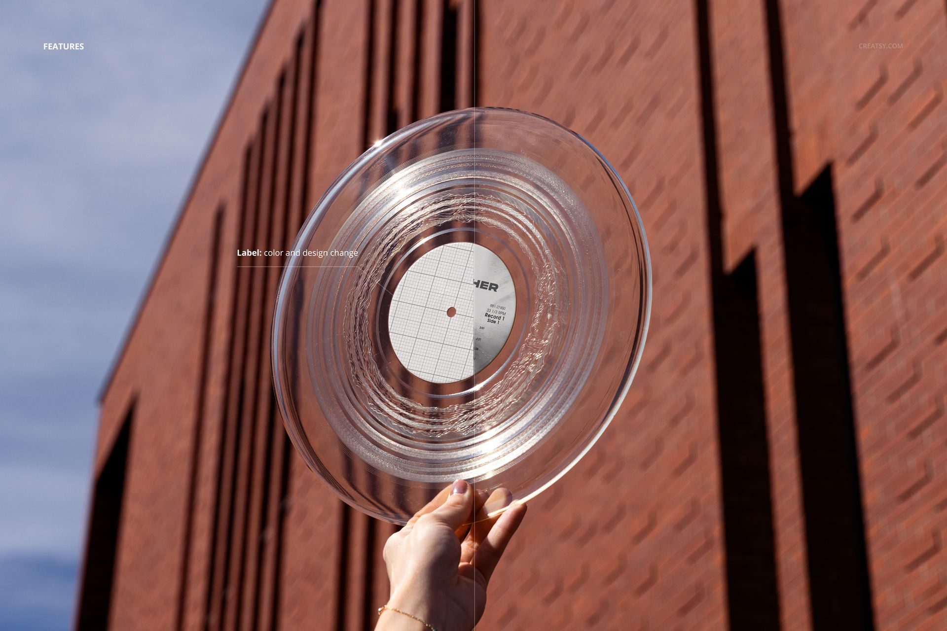 Transparent vinyl record mockup being held in one hand with a modern brick wall background in daylight.
