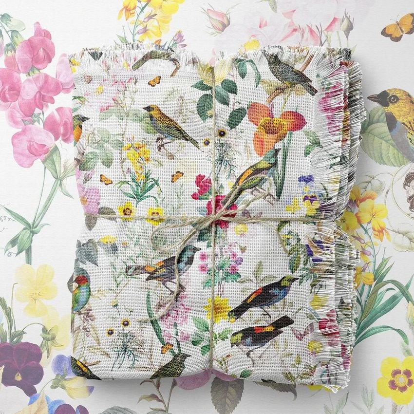 Polyester woven coverlet mockup featuring a folded blanket with a colorful bird and floral pattern, tied with twine, placed on a matching floral background.