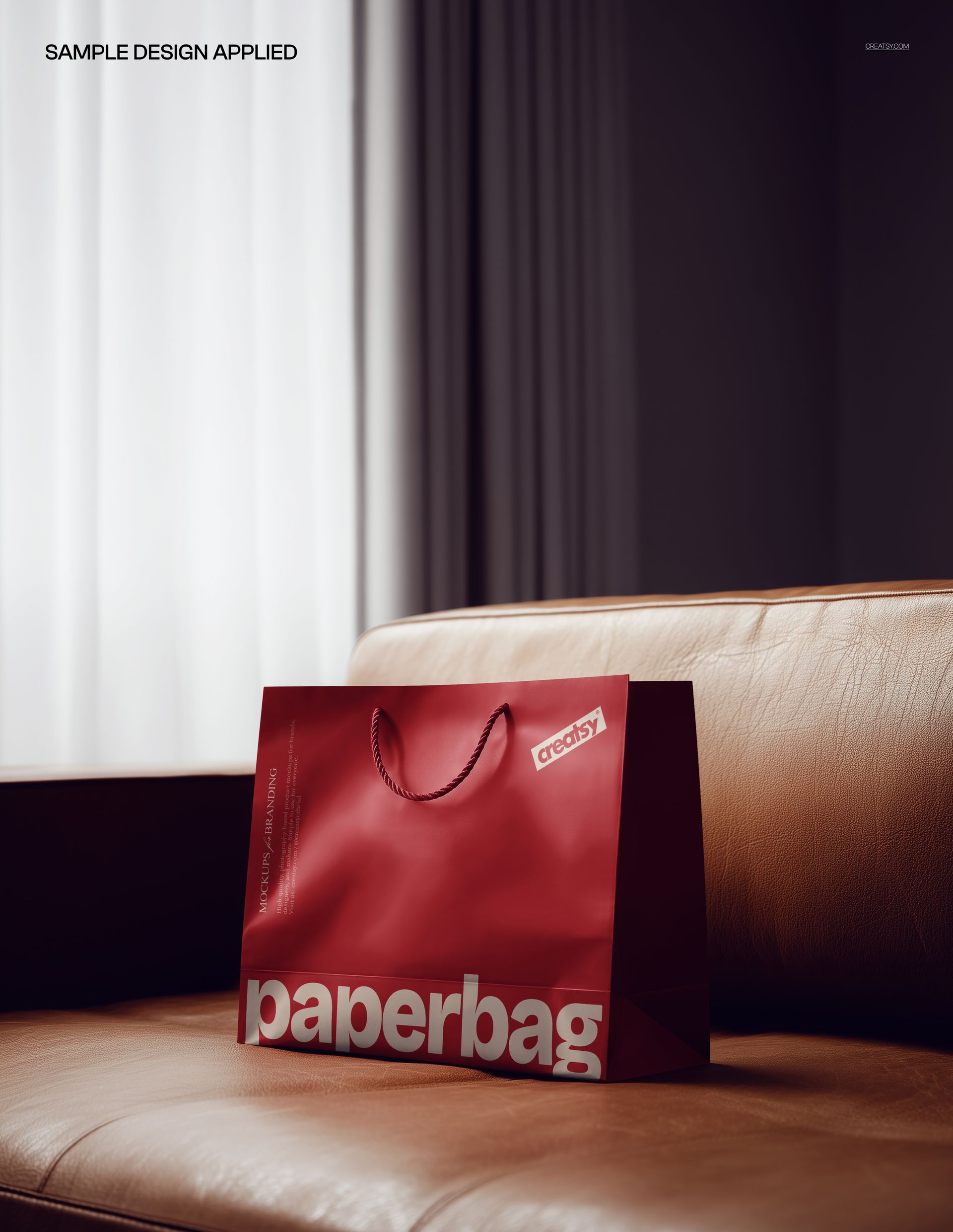 Premium paper bag mockup featuring a glossy red bag with bold text, placed on a light brown leather sofa.