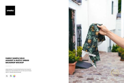 PSD mockup showing a fabric piece with green and orange botanical design, held outdoors in a city courtyard.