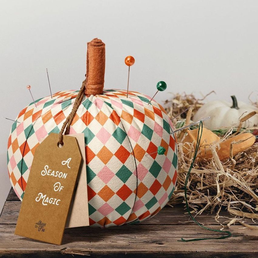 Fabric pumpkin mockup featuring a geometric diamond pattern in orange, green, and cream, with pins and a brown paper tag attached.